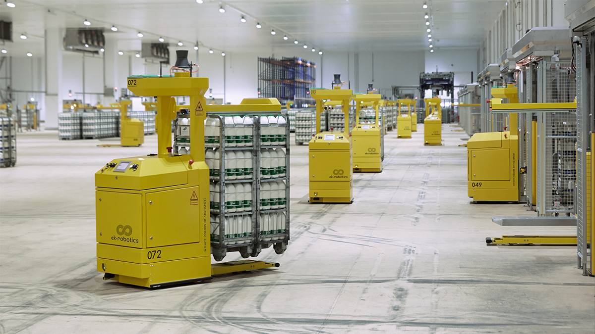Eine industrielle Lagerhalle oder ein großer, heller Raum mit mehreren gelben autonomen mobilen Robotern (AMRs), die unterschiedliche Gegenstände transportieren. Die Umgebung wirkt modern und geräumig.