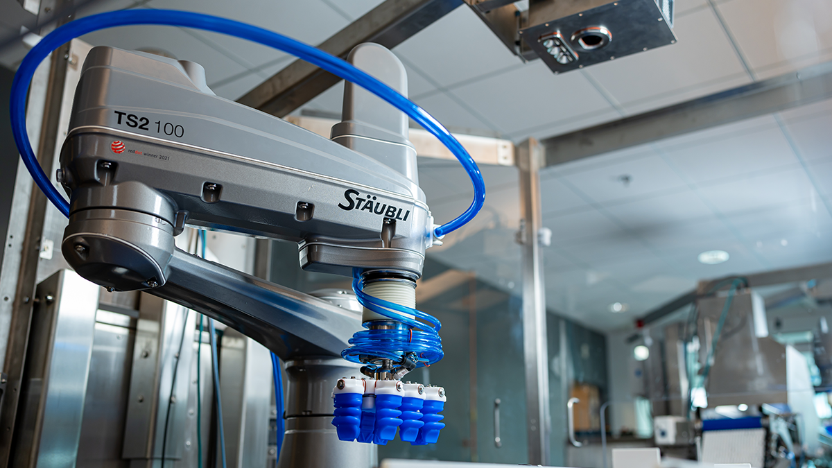 Eine industrielle Maschine, vermutlich ein Industrieroboterarm der Marke Staubli, ist in einer Fertigungsstätte installiert. Es handelt sich um eine hochentwickelte, automatische Produktionsmaschine in einem industriellen Umfeld.