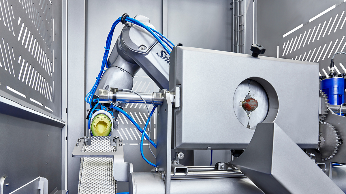 Eine hochpräzise, automatische Maschine bearbeitet ein Stück Obst, wahrscheinlich eine Avocado. Diese Anwendung zeigt spezialisierte Robotik im Bereich der Lebensmittelverarbeitung oder -veredelung.