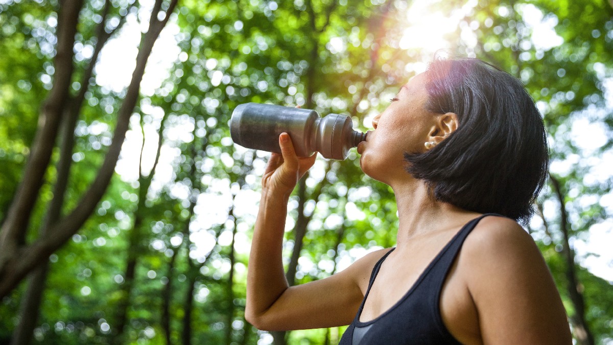 Woman drinking from a sports bottle in the forest.