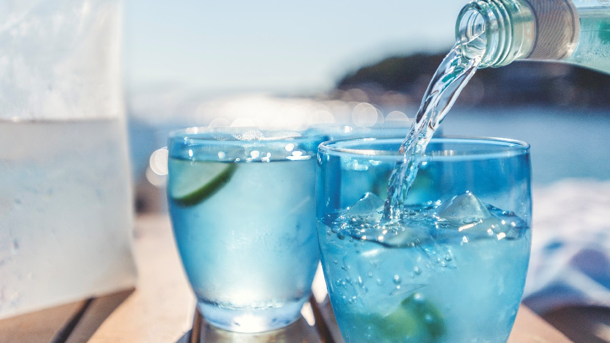 Water is poured into a glass with the sea in the background.