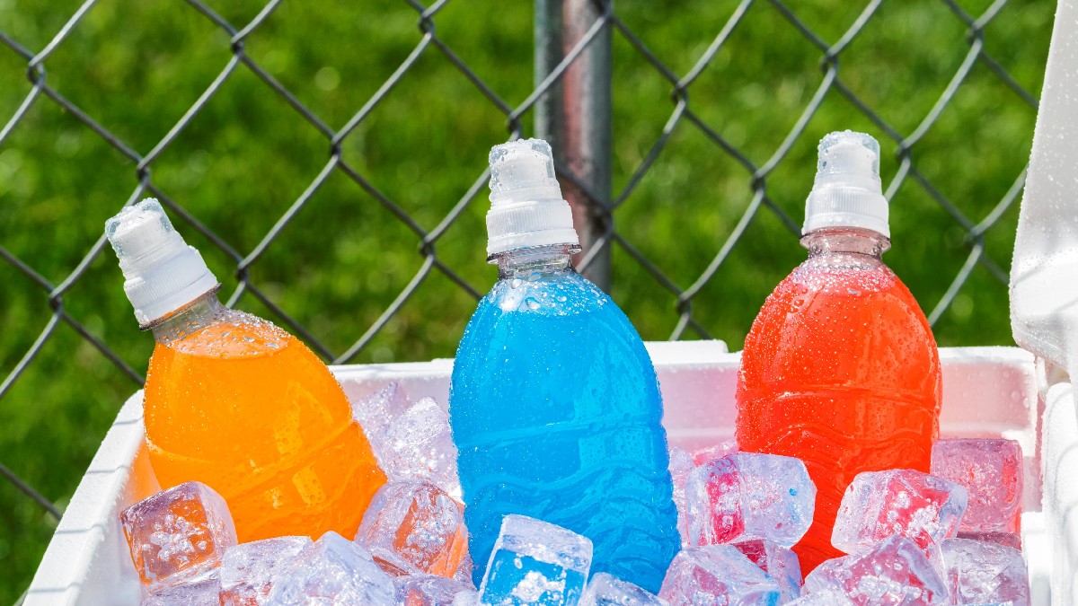 Three bottles of orange, blue and red drink lie in a box with ice.