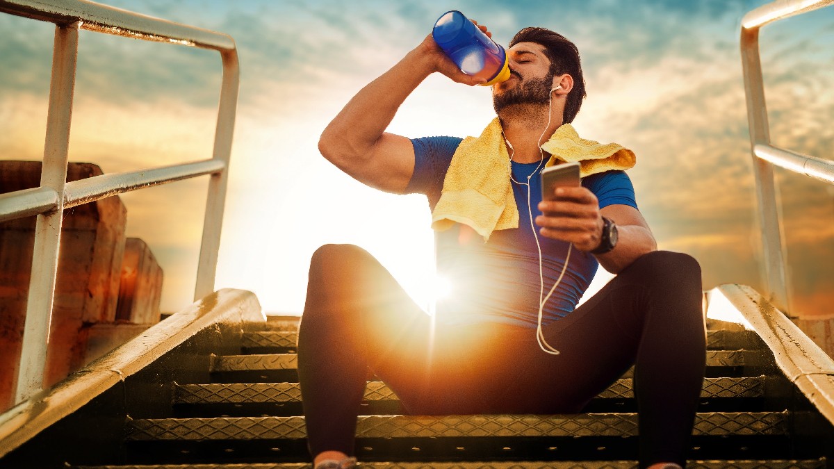 Man sitting on a staircase in sportswear, drinking from a sports bottle in the sunset.