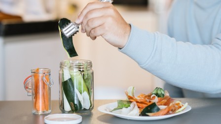 Ein Mensch legt Gemüseschalen in ein Weckglas zur Fermentierung