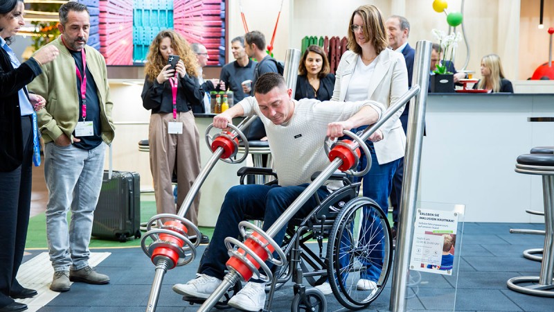 Special exhibit "The Inclusion Trail" – person in a wheelchair and children using an accessible play structure outdoors. A lively and inclusive atmosphere in a park with green surroundings.
