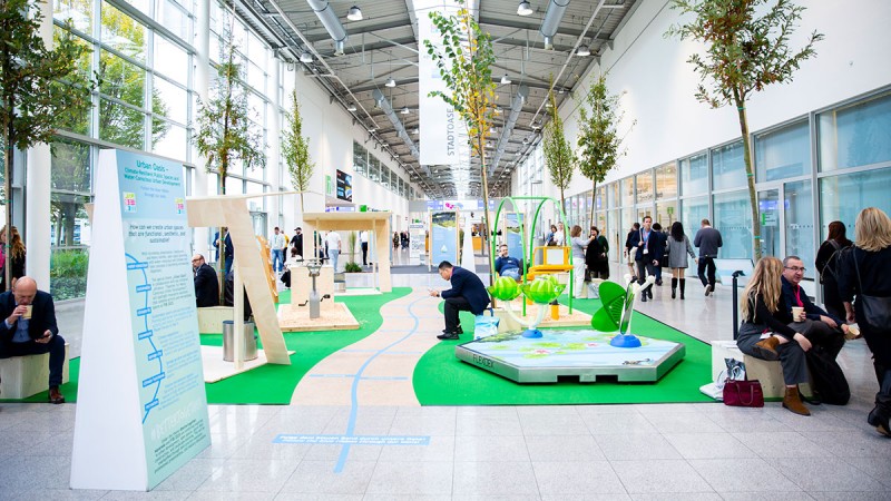 Urban park with playgrounds, basketball court, lots of trees and people of different ages playing and moving around