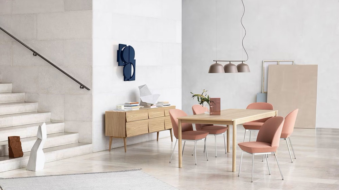 Modern, bright dining room with a wooden table, six pink upholstered chairs, a sideboard, and minimalist decor.
