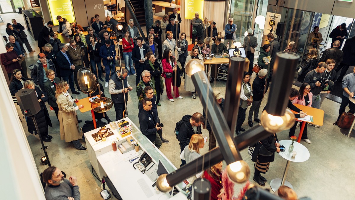 A crowd gathers in a modern indoor space with tables and lighting to attend an event.