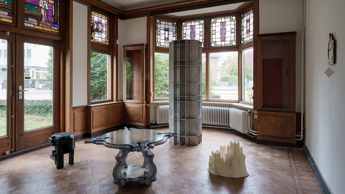 Artworks displayed in a historic room with large windows and wooden floors.