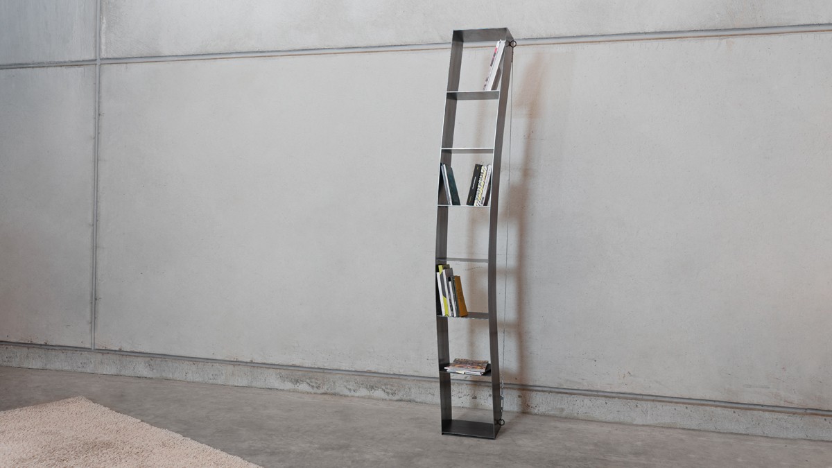 Slim, curved metal shelf in front of a grey wall.