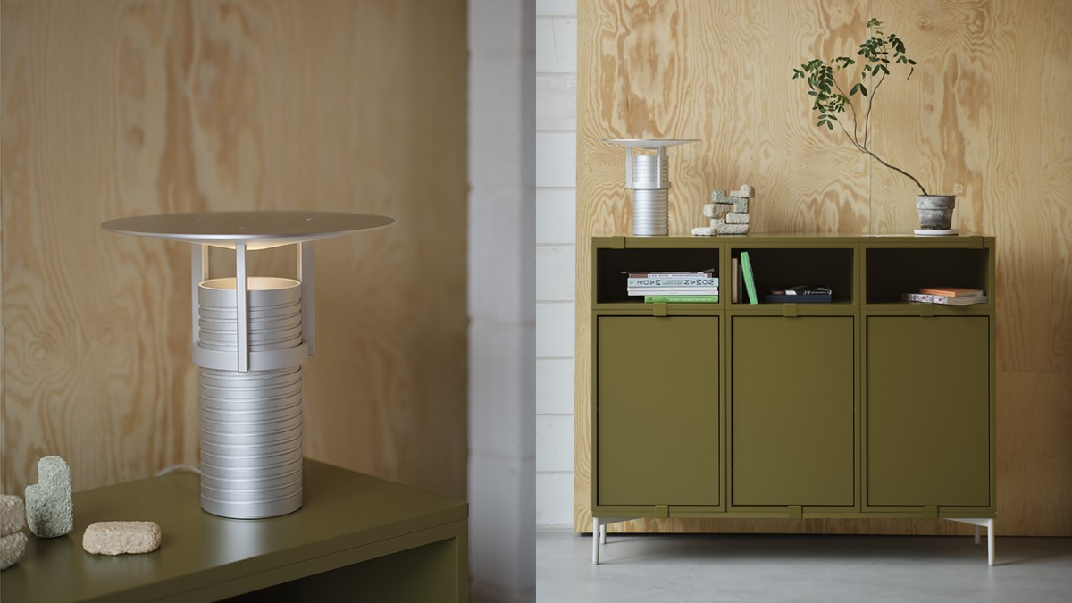 Modern silver table lamp with a round shade on an olive green sideboard in front of wood paneling.