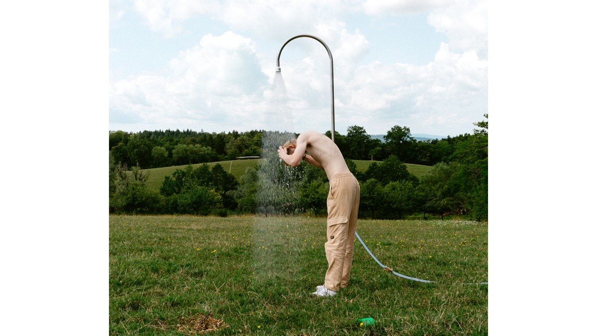 A person washes their hair under a garden shower.