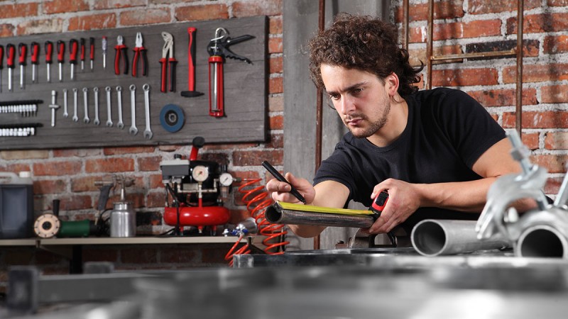 Workbench in a workshop with tools hanging on the wall, a helmet, a tire, and several boxes underneath.