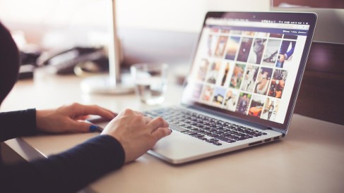 Person sitzt vor einem aufgeklappten Laptop und schaut sich Fotos an