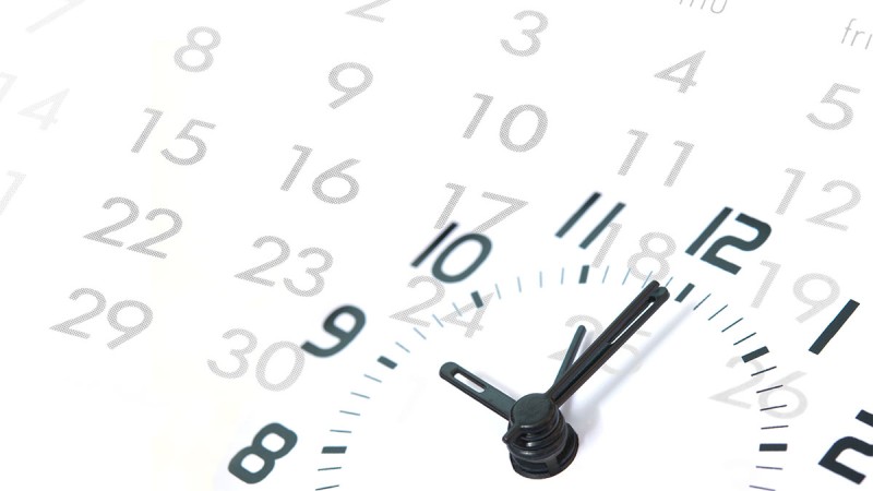 Clock with black numerals and hands, with a calendar in the background
