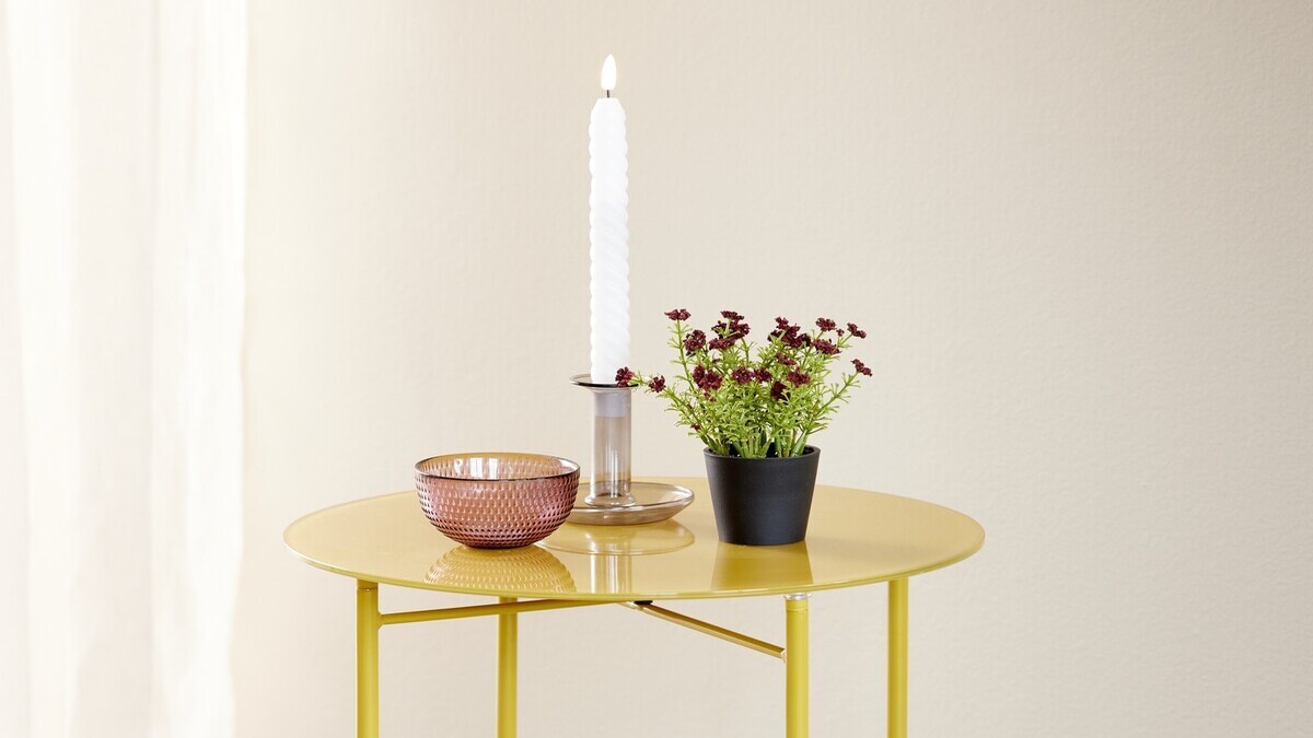 A yellow table with a candle in a holder, a small potted plant and a decorative bowl.