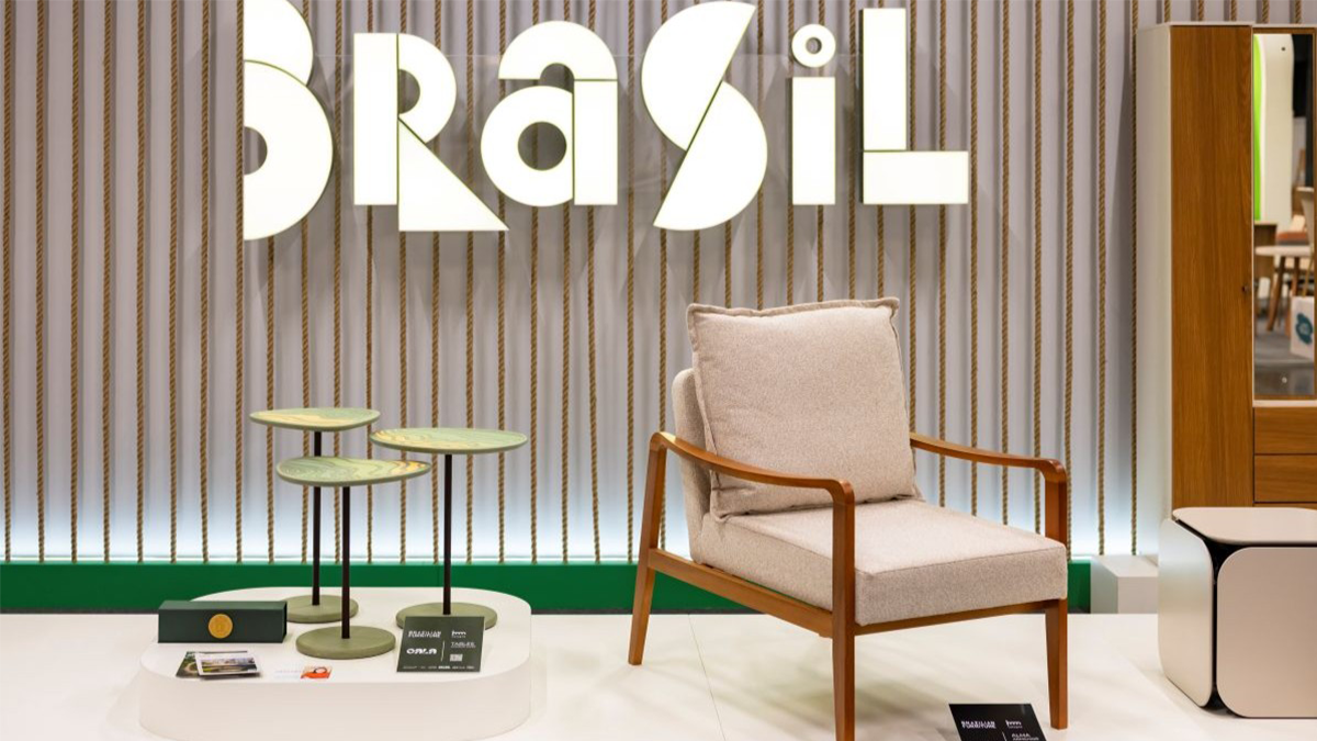 Impression von der imm cologne: Modern gestalteter Messebereich mit einem gemütlichen Polstersessel, drei kleinen Tischen und großem „Brasil“-Schriftzug im Hintergrund.