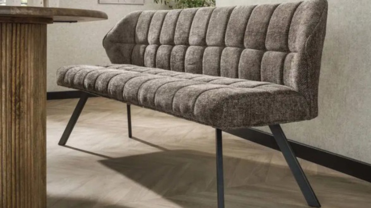 Graue gepolsterte Sitzbank mit modernen Metallbeinen, platziert auf einem hellen Holzboden neben einem Holztisch.