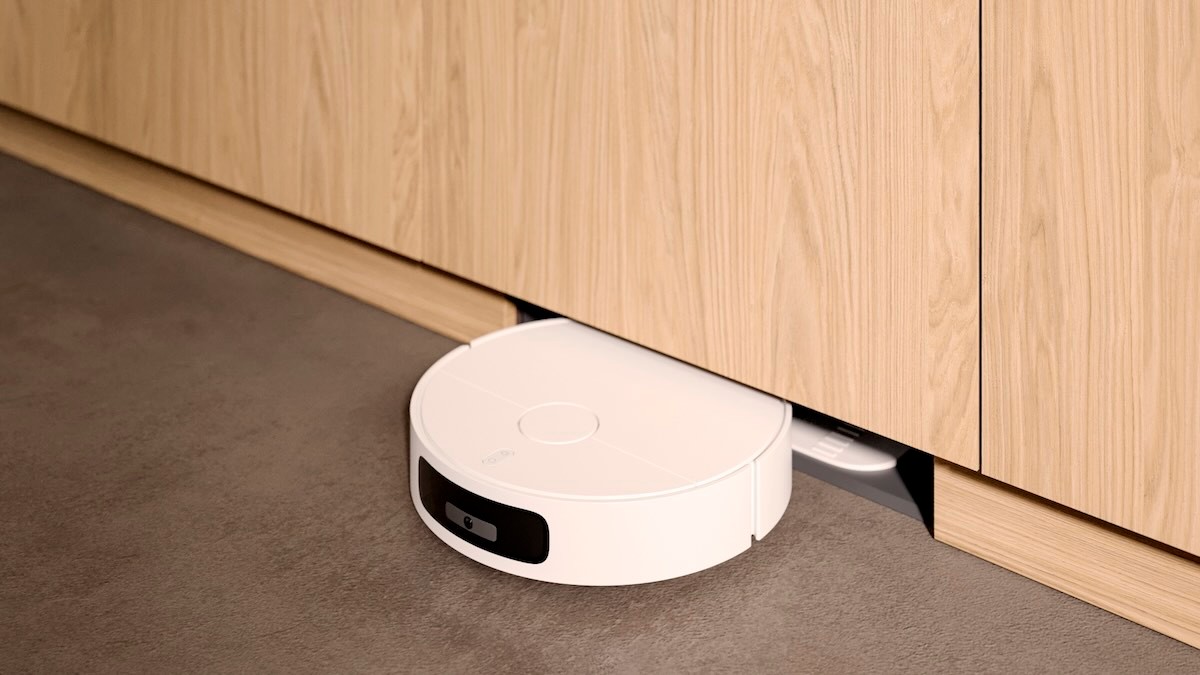 A robot vacuum cleaner drives under a cabinet between two trim strips