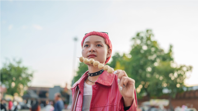 A young woman with pink hair and a pink jacket holding a skewer of sweets in her hand.