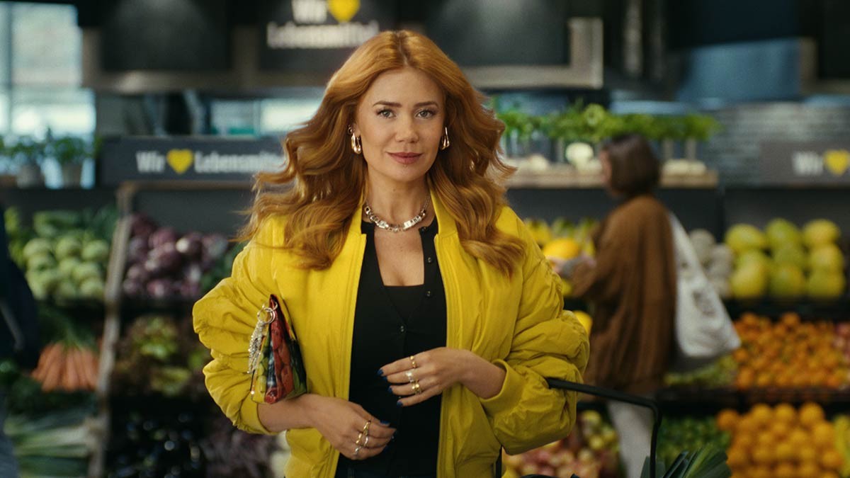 Palina Rojinski walks through Edeka’s produce section, with fruit and vegetables in the background.