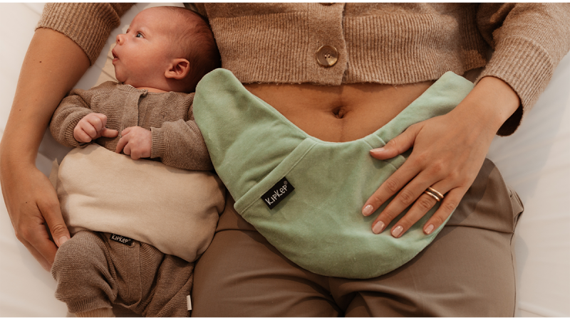 Adult and baby lying down with Lexie brand heating pillows on their stomachs, adult wearing brown cardigan and pants, baby in brown outfit