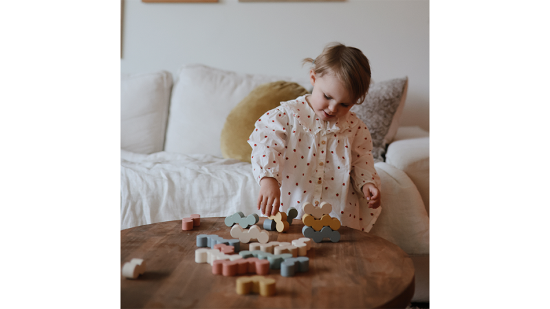 Child playing with wooden balance blocks shaped like animals on a round wooden table in a living room