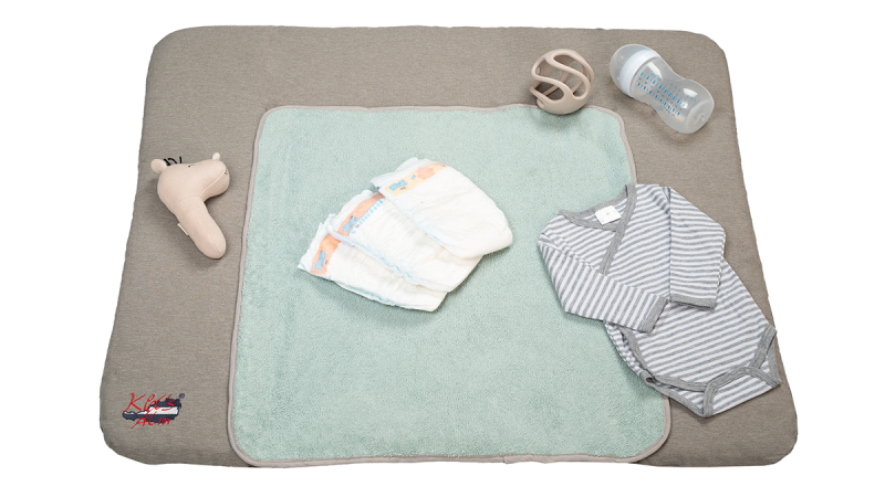 Osann baby changing mat with soft beige and mint green layers, diapers, striped gray baby bodysuit, baby bottle, and beige teething toy