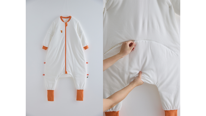 White baby sleep suit with orange cuffs and zipper, shown flat and being stretched at the waist
