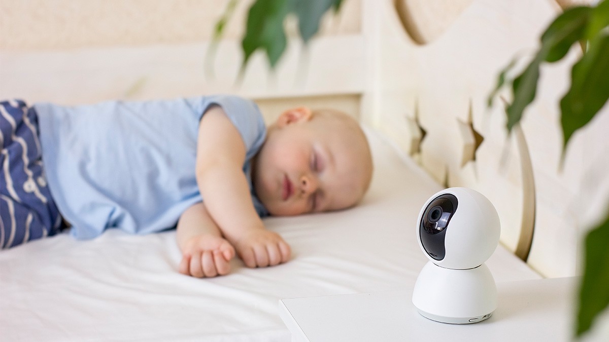 Das digitale Babyzimmer: Baby liegt schlafend im Bett und wird von Kamera überwacht.