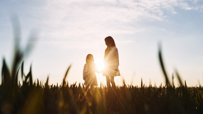 Frau und Kind stehen im Sonnenuntergang auf einer Wiese