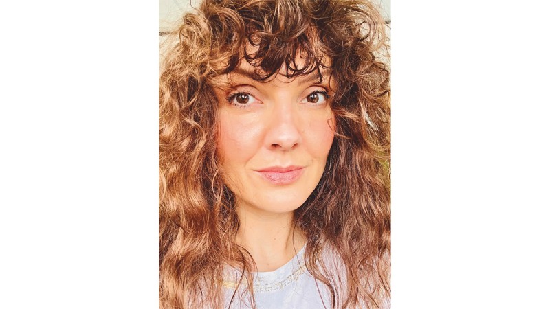 Person with long, curly brown hair wearing a white shirt with lace detail at the neckline.