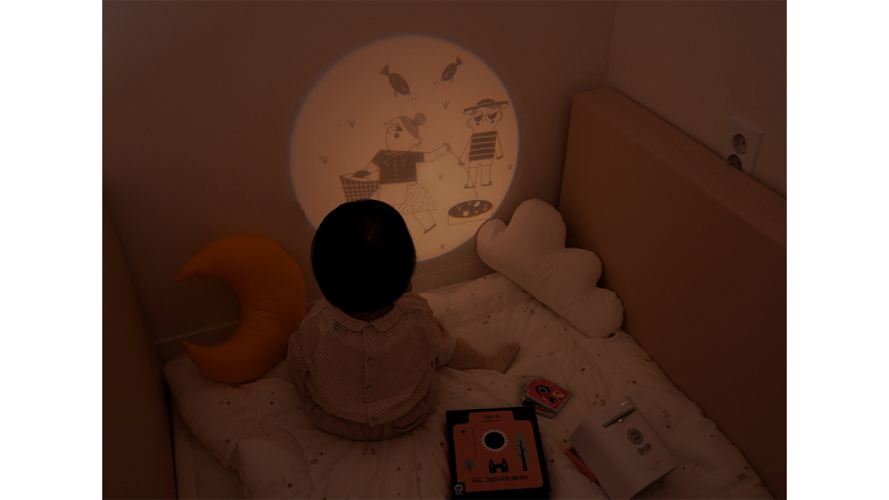 Child sitting on bed watching shadow puppets of animals and people projected on wall