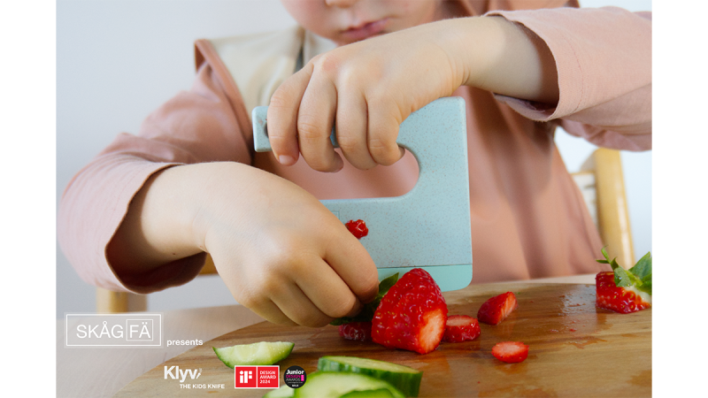 Child slicing strawberries and cucumber on a wooden board with a blue kitchen tool