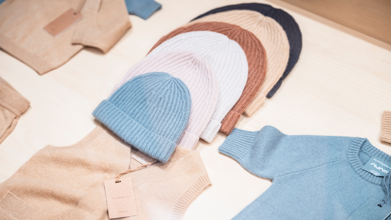 A row of children's clothing hangs on hangers attached to a metal rail. The garments are in various pastel colors and patterns, including stripes, floral prints, and solid colors. The selection is diverse, colorful, and suitable for young children or babies.