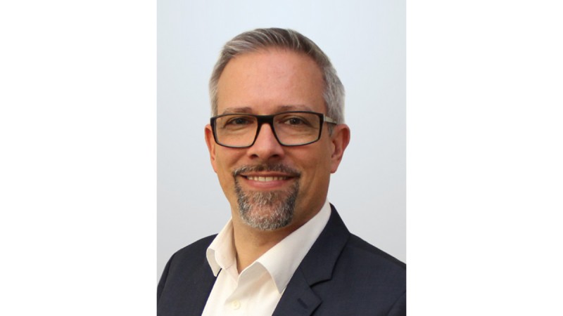 Man with glasses, gray hair, and beard smiling in a portrait, wearing a suit and white shirt.
