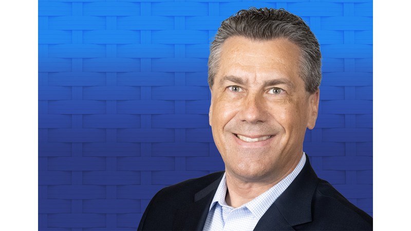 Portrait of a smiling man in a suit against a blue woven-pattern background.