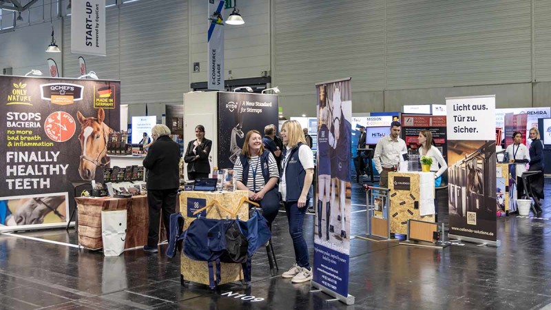 Messestand auf der spoga horse mit Werbebannern für Pferdezahnpflege und mehreren Personen im Gespräch